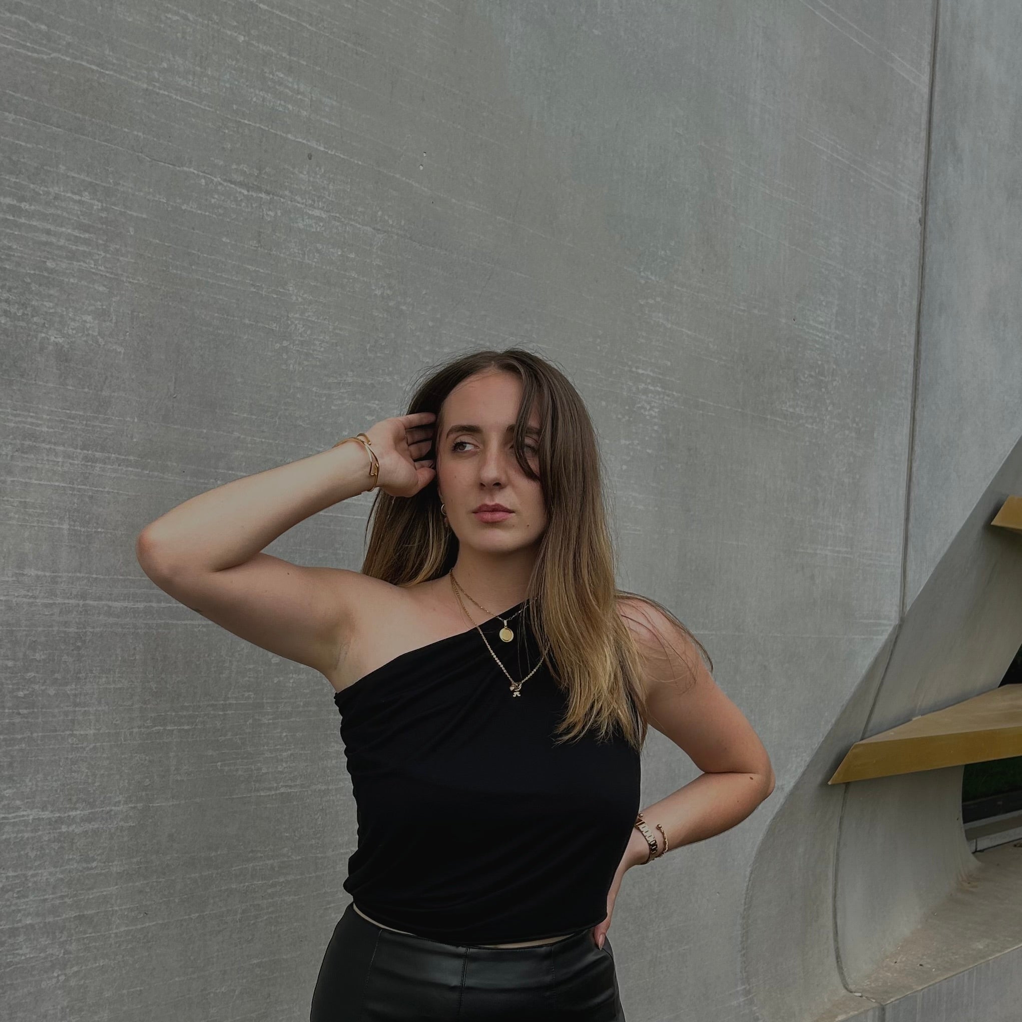 Portrait de face d'une femme posant avec le haut ajustable noir de la marque Bonjour Leoni en col asymétrique.